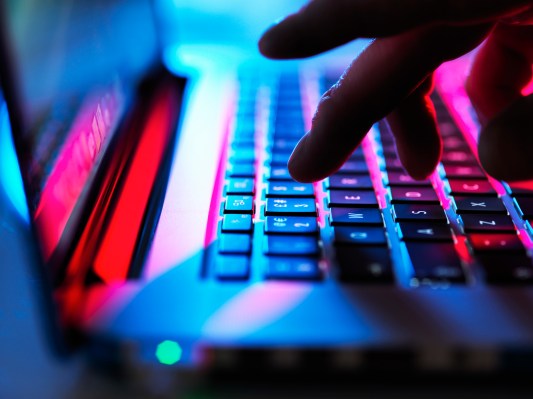 Fingertips typing on a laptop computer under red and blue lights