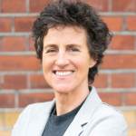 Portrait of Ellen Sprenger wearing a light blazer and dark shirt against a brick wall background.