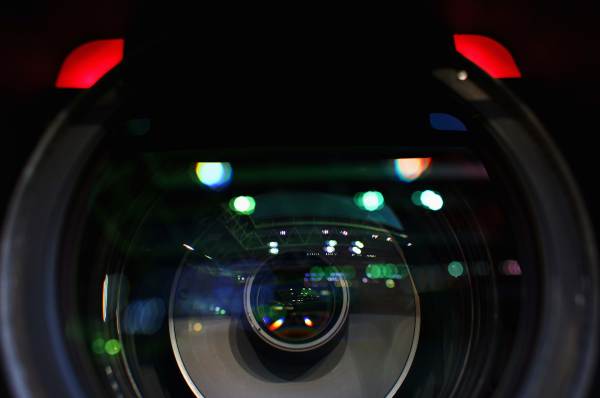 A closeup image of a video camera lens shows colorful reflections.