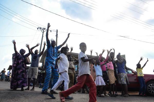 On a sunny day in Owo, Nigeria, young people raise their hands, many smiling, as they briskly march down the street.