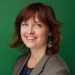 Portrait of Amy Kenyon wearing a grey blazer and black top against a green background.