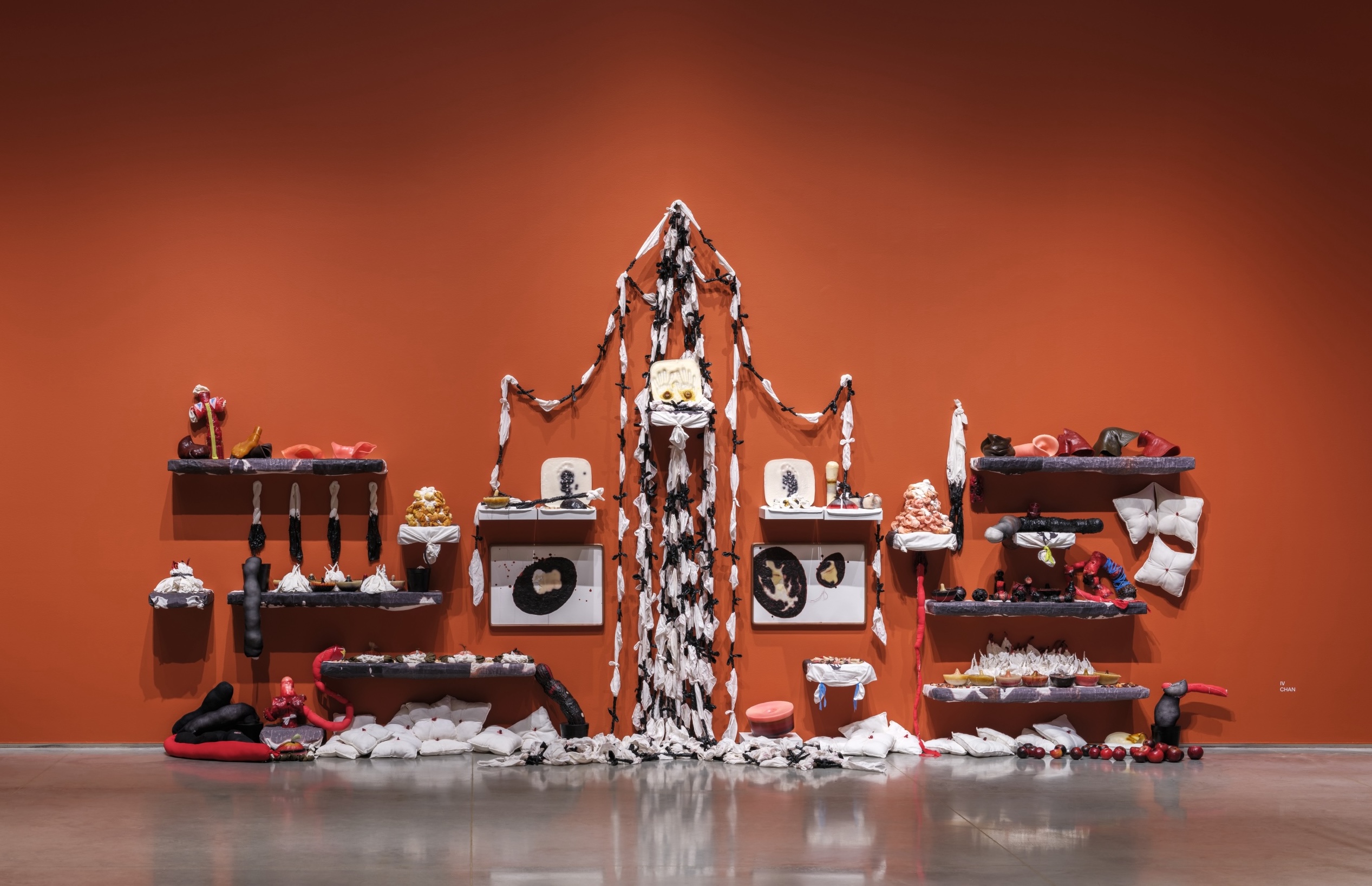 Mixed media installation resembling a shrine with soft sculpture, pillows, fabric chains, and wax molds.
