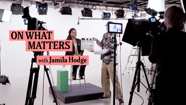 A studio setup shows a woman sitting on a stool with a clapperboard in front of her. The text "On What Matters with Jamila Hodge" appears on the left side. Cameras, lights, and other equipment surround her, indicating the start of a video production.