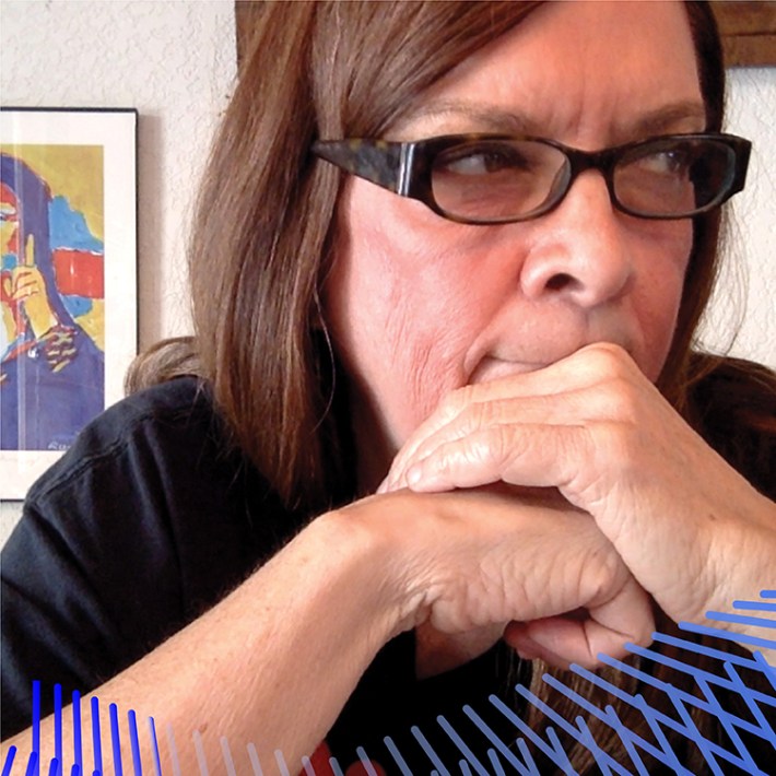 Nancy, a woman with long brown hair and glasses, holds her hands to her face, and looks off camera. Behind her is a rendition of the Mona Lisa in primary colors.