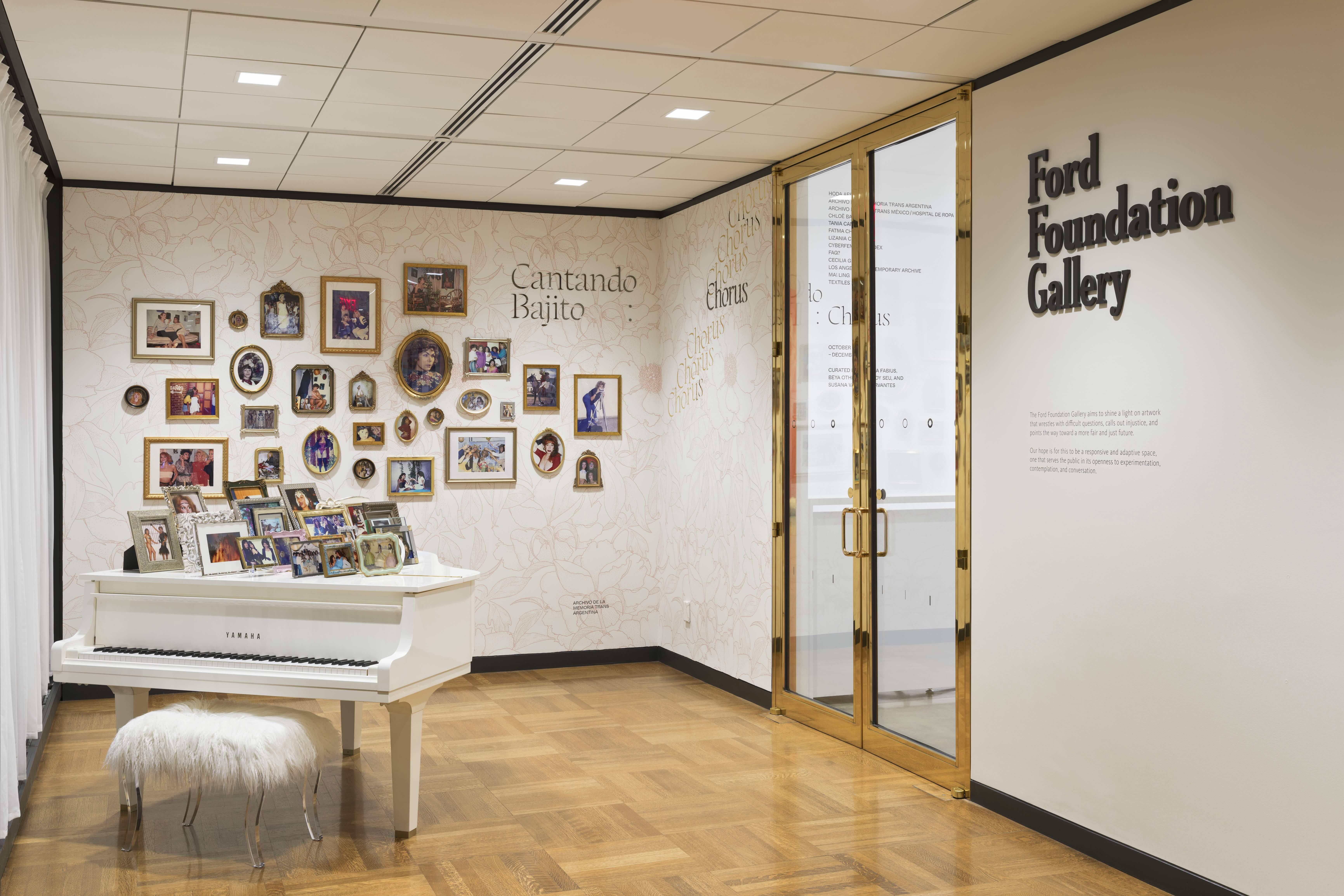 Installation of a grand piano with framed photos on the lid and on the wall behind it.