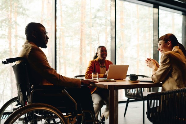 A businessman in a wheelchair is discussing with coworkers at a conference table in a convention center.