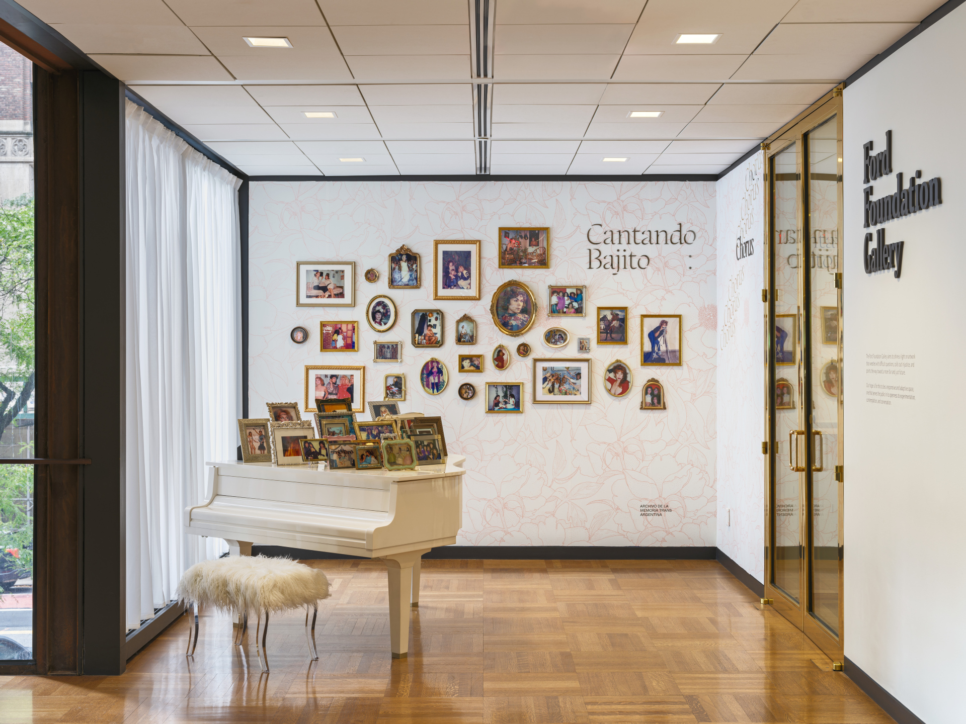 Installation of a grand piano with framed photos on the lid and on the wall behind it in front of a gallery entrance.