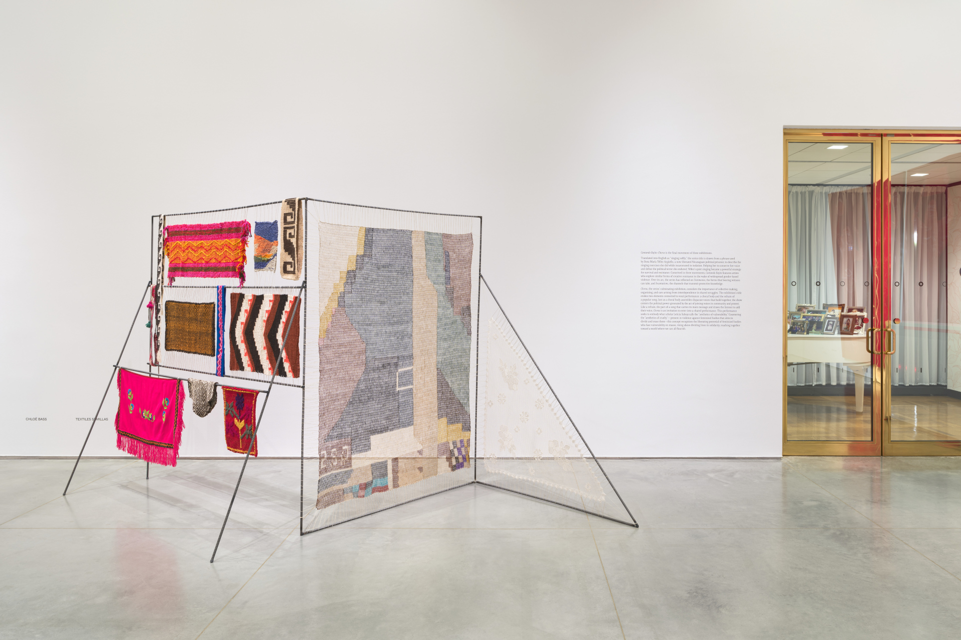 Gallery wall with a zigzag shaped metal frame holding irregularly sized textiles and clear gold-framed entrance doors.