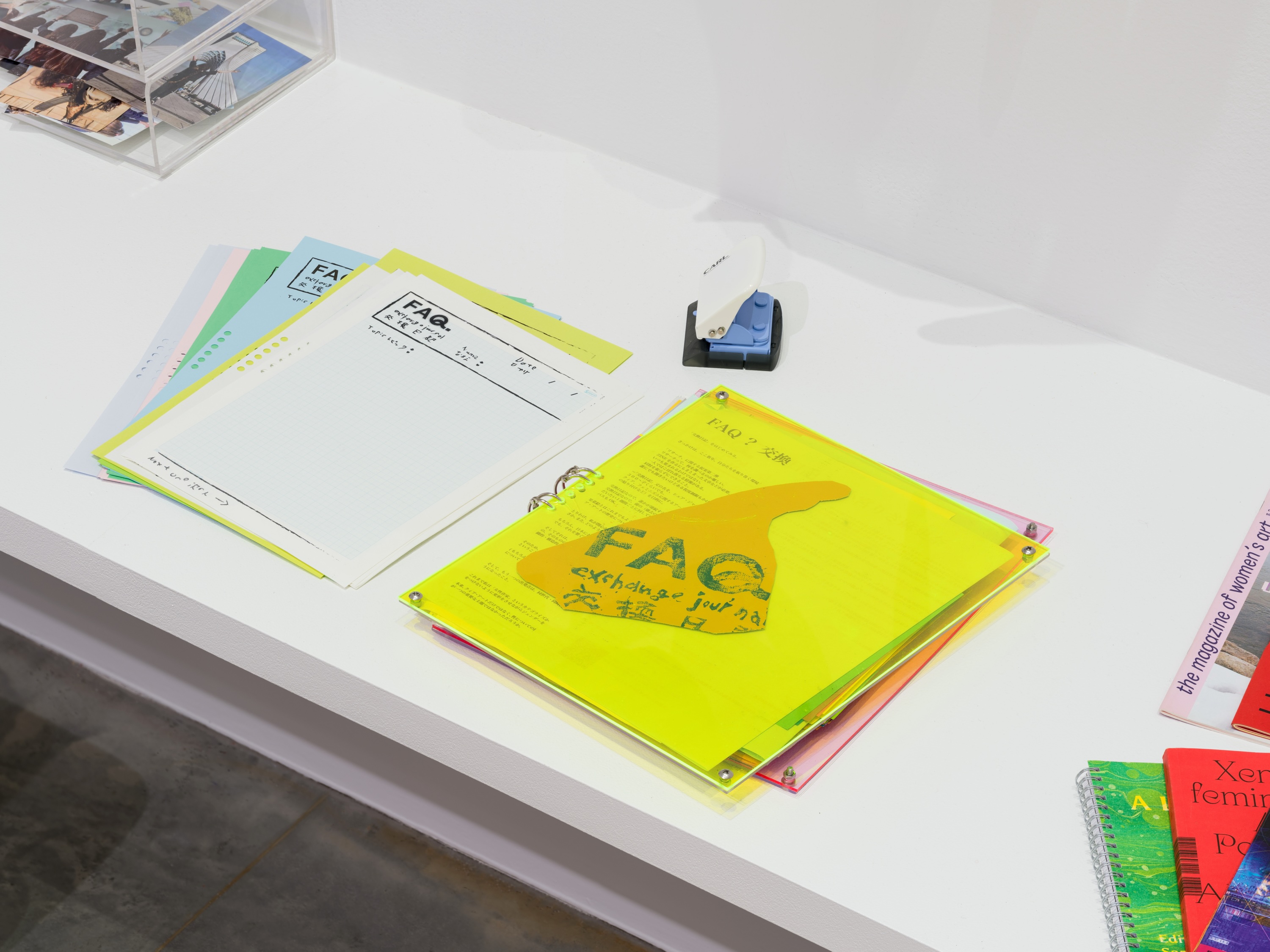 Bound pamphlet, loose leaf journal pages, and a miniature hole punch on a white desk.