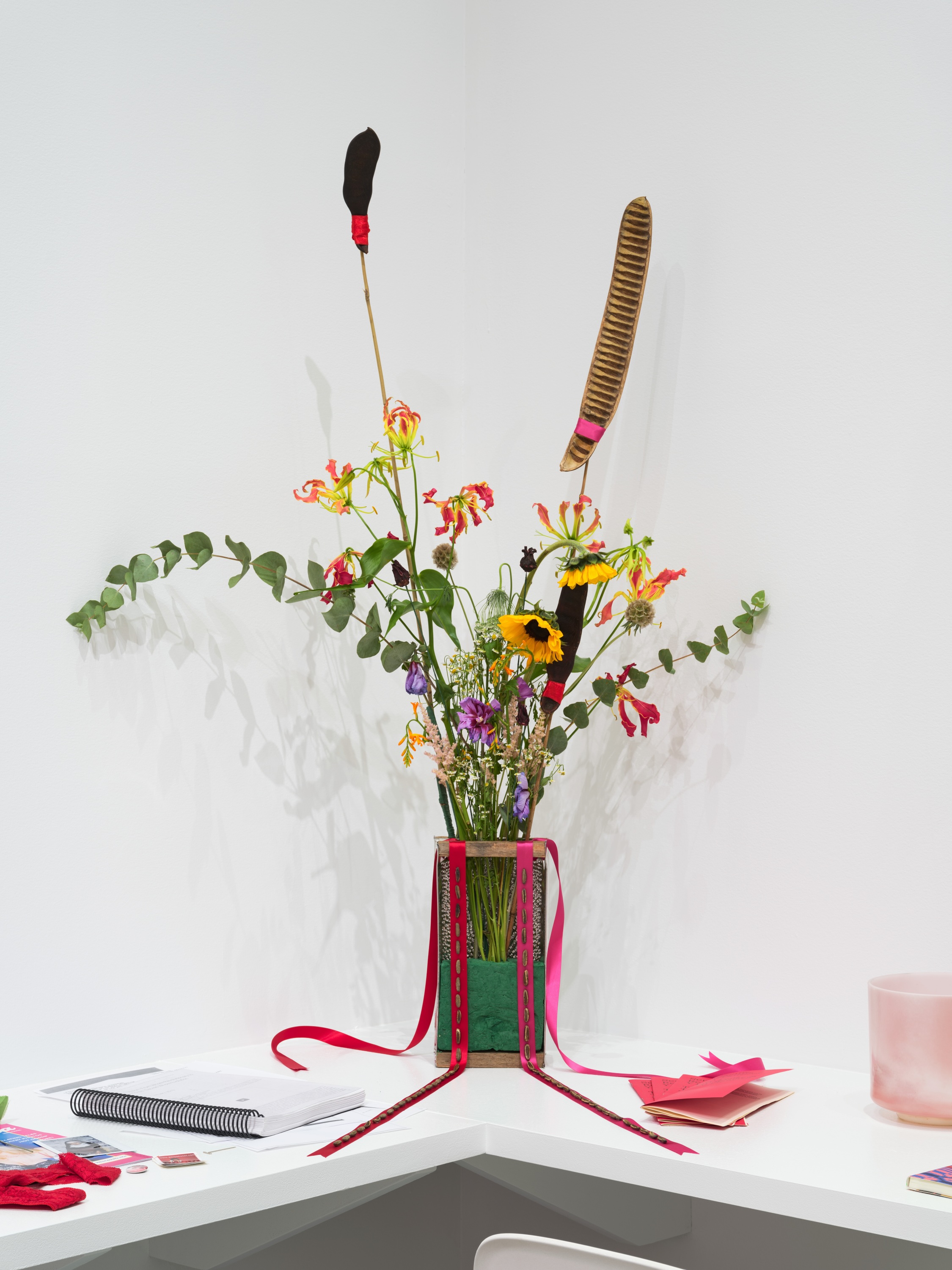 Floral arrangement in a glass vase decorated with ribbons and a stack of red pamphlets.