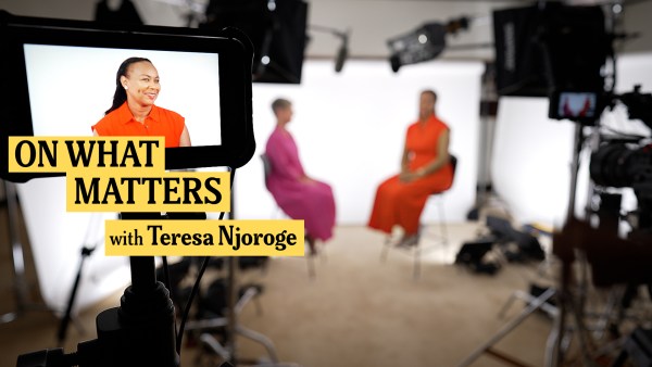 A brightly lit studio setup showing Teresa Njoroge in orange seated opposite Hilary Pennington in pink. The scene is framed by cameras and lighting equipment. The text On What Matters with Teresa Njoroge overlays the image.