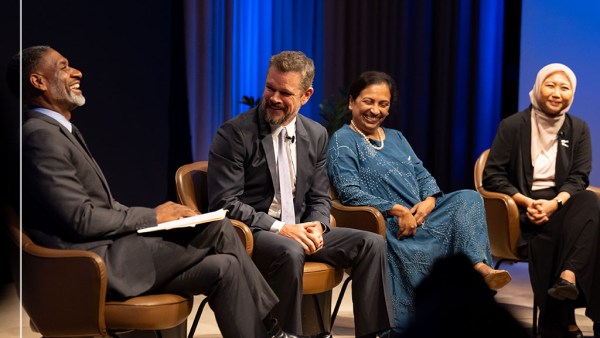 Four individuals, two men and two women, dressed in business casual and formal attire, are sitting in conversation against a blue curtain background. The women are smiling; one wears a hijab. The men are also smiling, both in suits and ties. From left to right, they are Charles Blow, Matt Damon, Vedika Bhandarkar, and Kiki Tazkiyah.